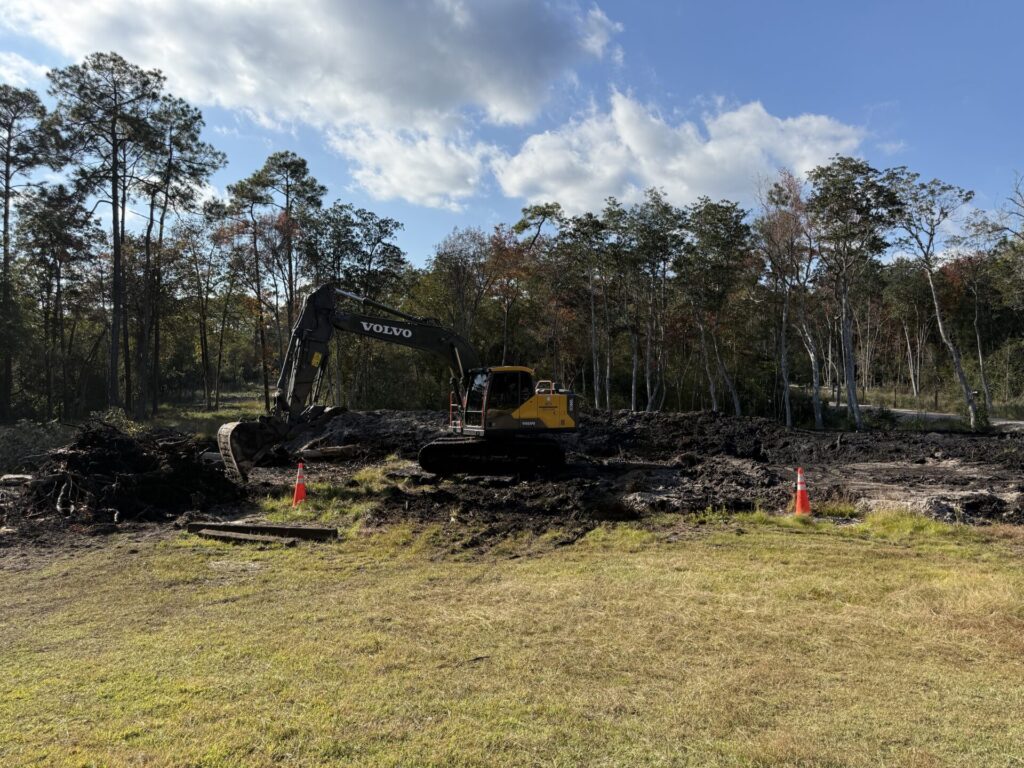 Excavator removing soil and debris during pond construction and land clearing in Pensacola.
